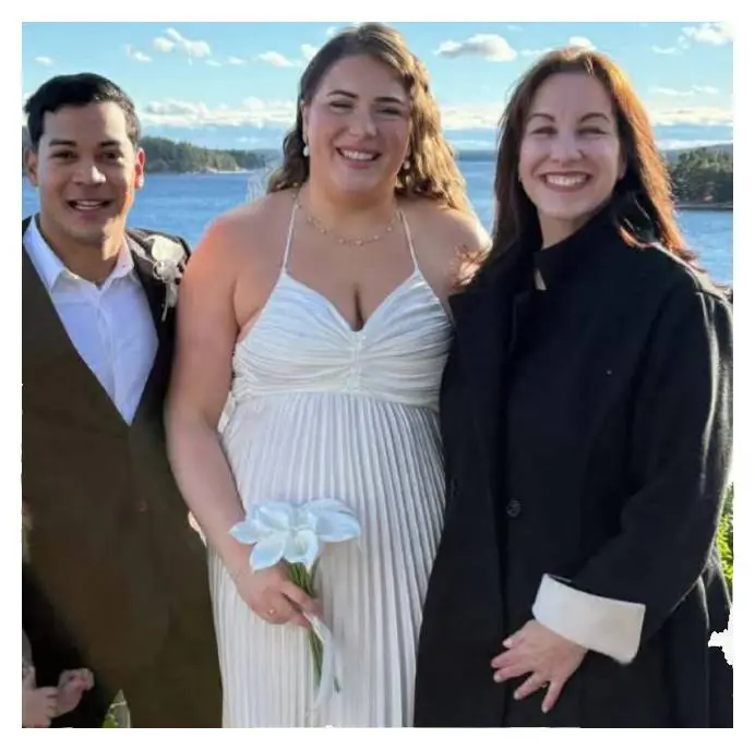 Three people posing outdoors near water on a sunny day.