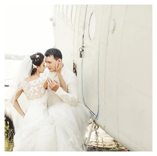 Bride and groom sitting by airplane fuselage.
